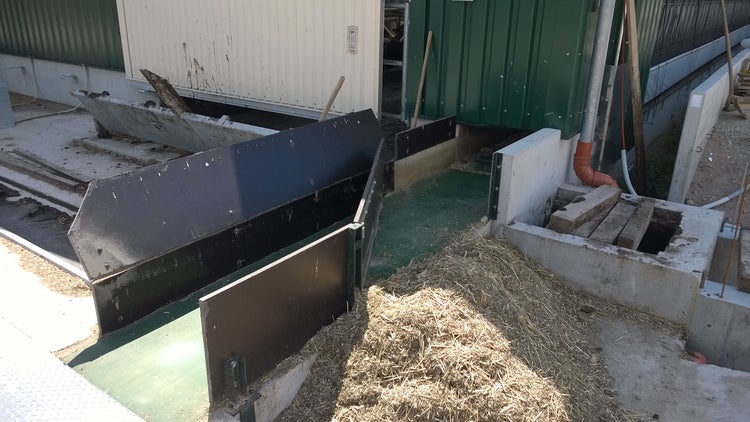 Detail close-up of aluminium flap edge pushing off remaining feed from belt into collection pit